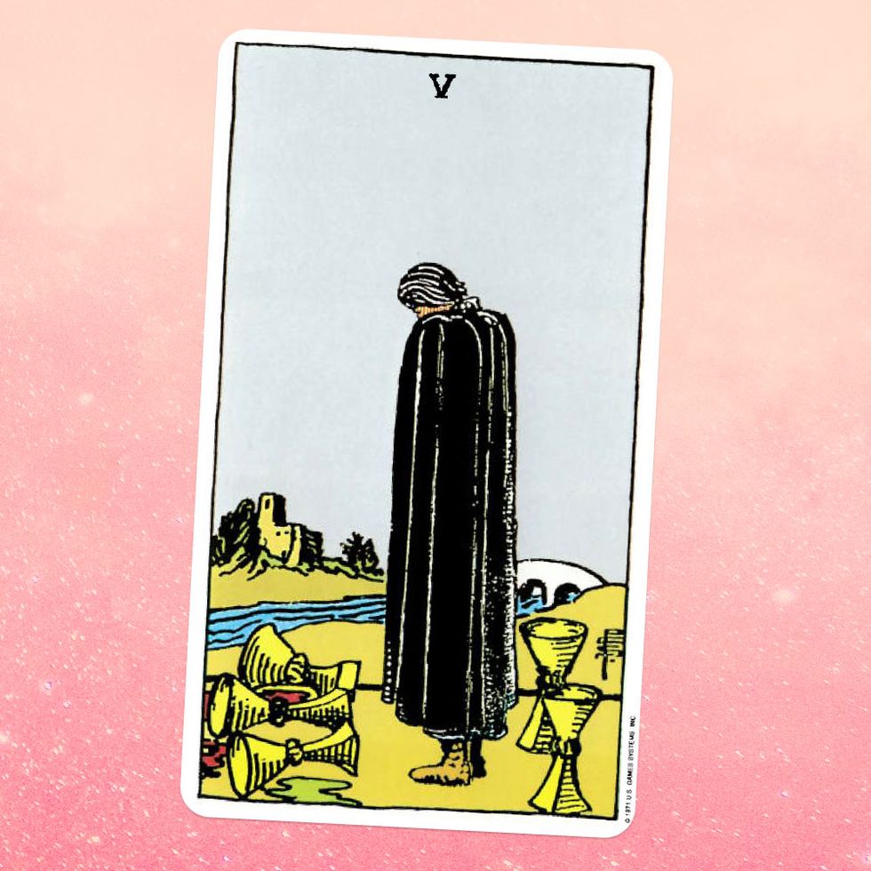 the tarot card the five of cups, showing a cloaked figure standing on a riverbank looking down into the water, with five cups spilled around them