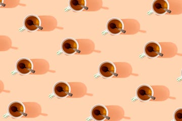 pattern of mugs of tea with spoons in them on peach colored background