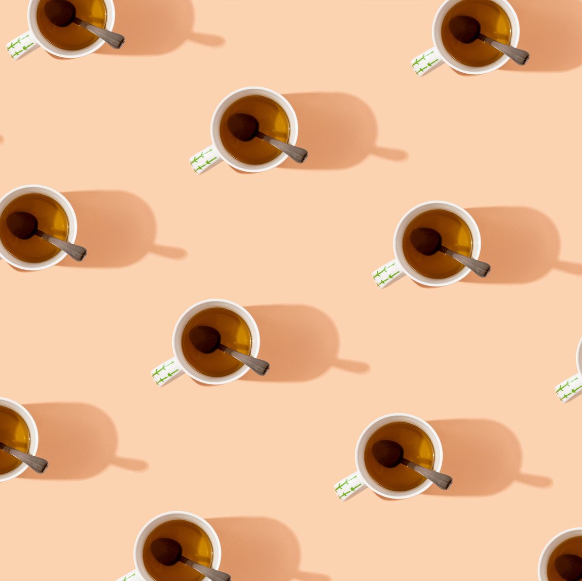 pattern of mugs of tea with spoons in them on peach colored background
