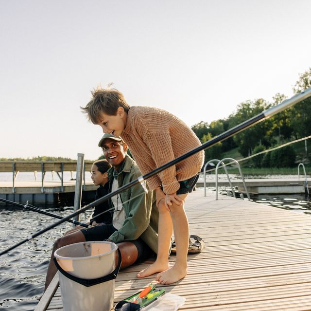 curious boy looking in lake with counselor doing fishing on jetty at summer camp