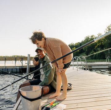 curious boy looking in lake with counselor doing fishing on jetty at summer camp