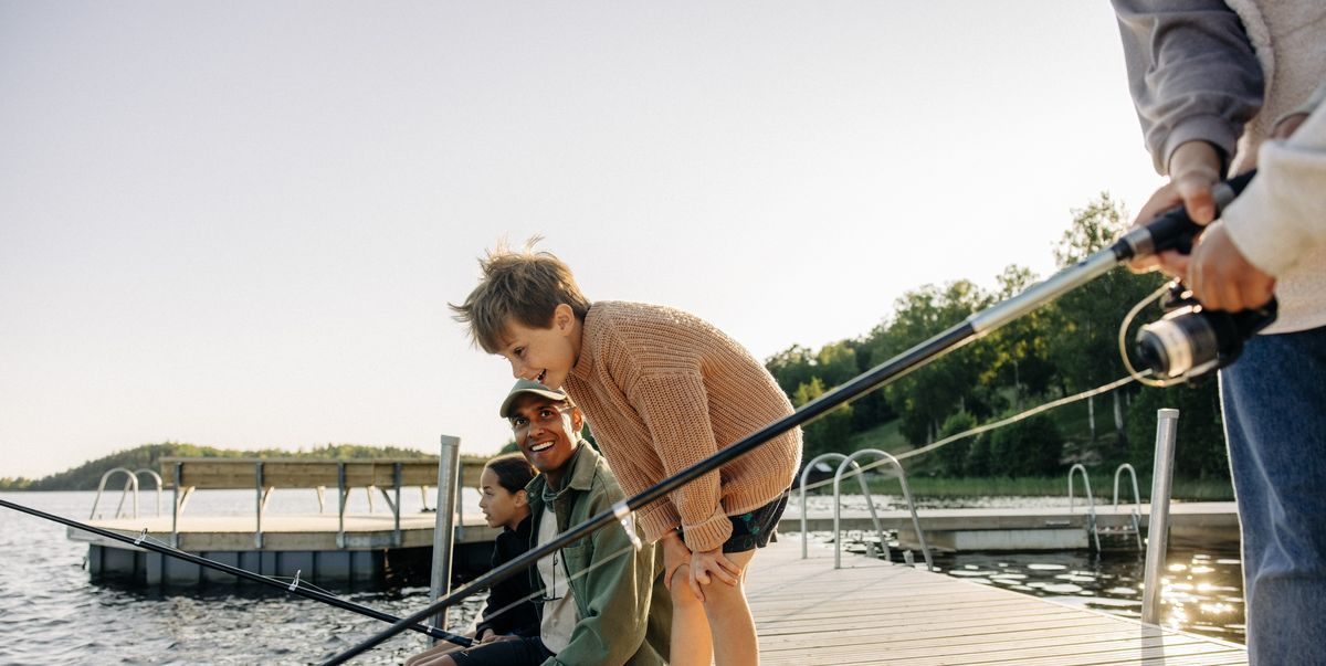 curious boy looking in lake with counselor doing fishing on jetty at summer camp