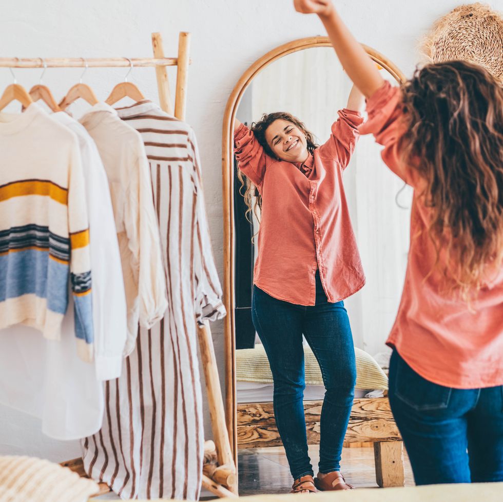 curly haired overweight young woman with satisfaction on face accepts curvy body shape standing near mirror