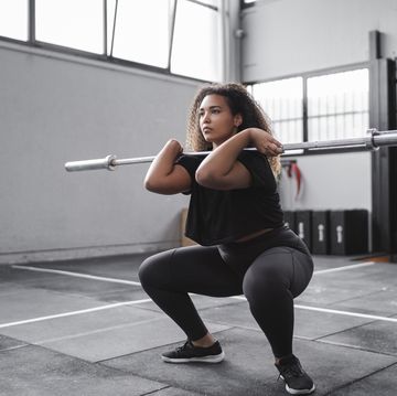 curly haired young woman practicing squats in gym