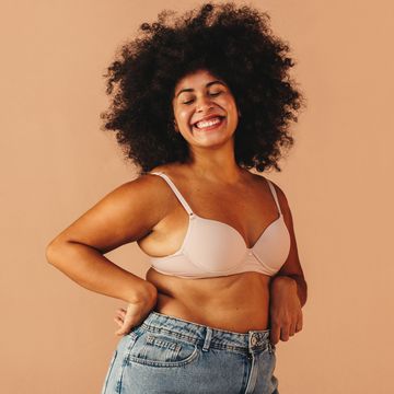 curvy woman smiling happily while wearing a bra and jeans