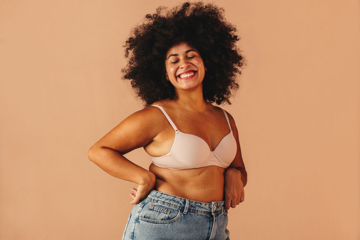 curvy woman smiling happily while wearing a bra and jeans