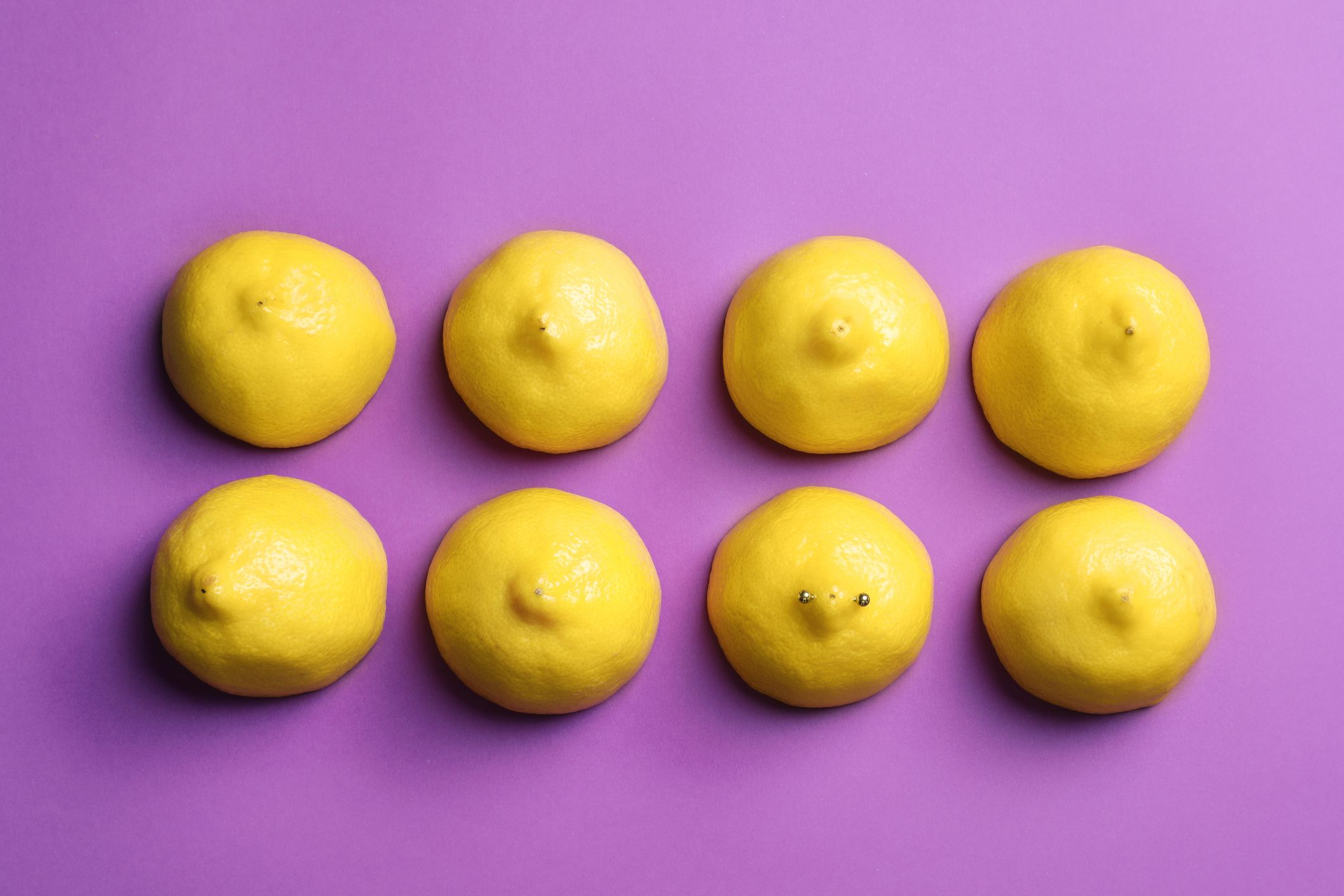 cut lemons symbolizing women's breasts and one with nipple piercing on purple background, flat lay