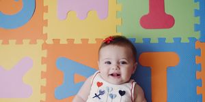 cute baby girl relaxing on colorful alphabetical puzzle playmat at home