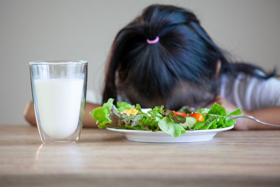 Cute Girl With Salad And Milk On Table Sitting Against Gray Background