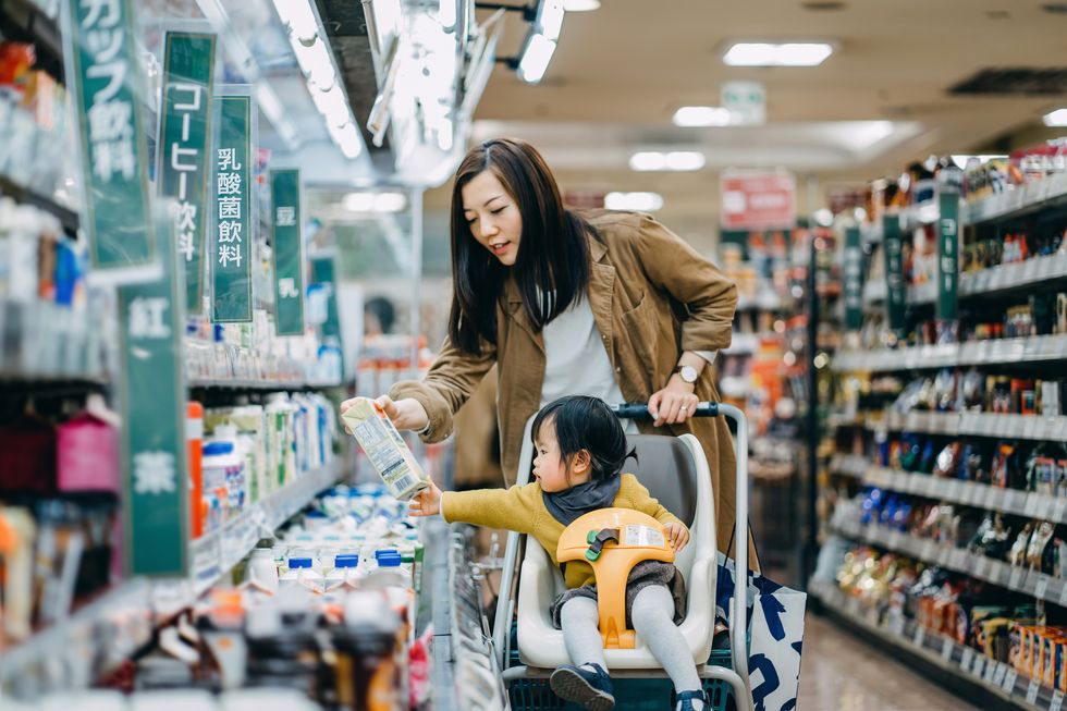 cute little daughter sitting in a shopping cart grocery shopping for dairy product with young asian mother in a supermarket