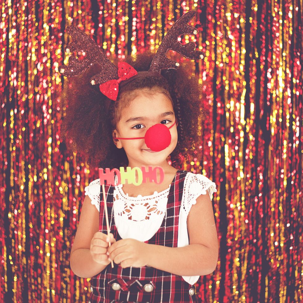 christmas activities cute little black girl wearing antlers and a red nose posing in front of a streamer wall