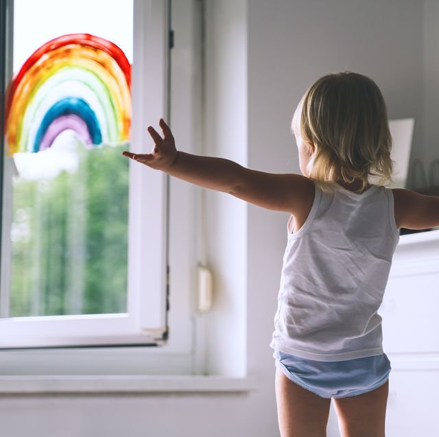 cute little girl having fun time jumping on bed on background of window with a painted rainbow