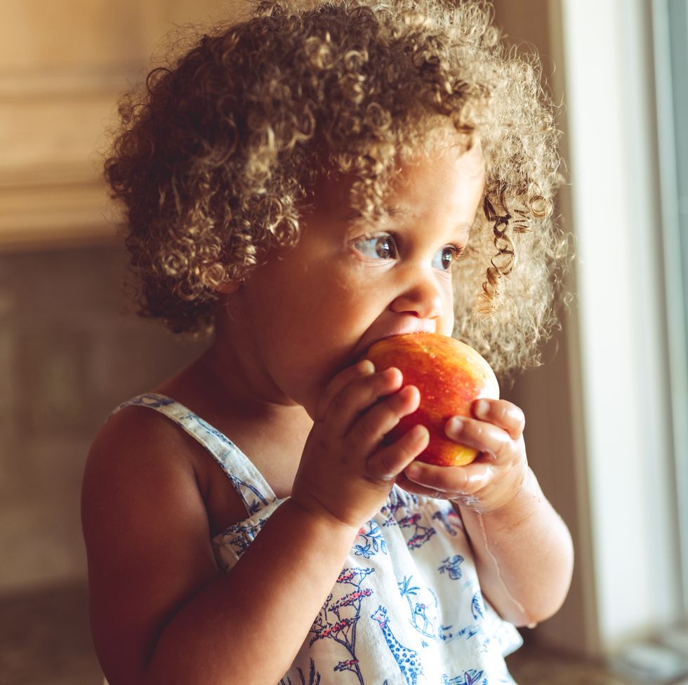 cute mixed race toddler girl eating a fresh red apple, healthy eating at home