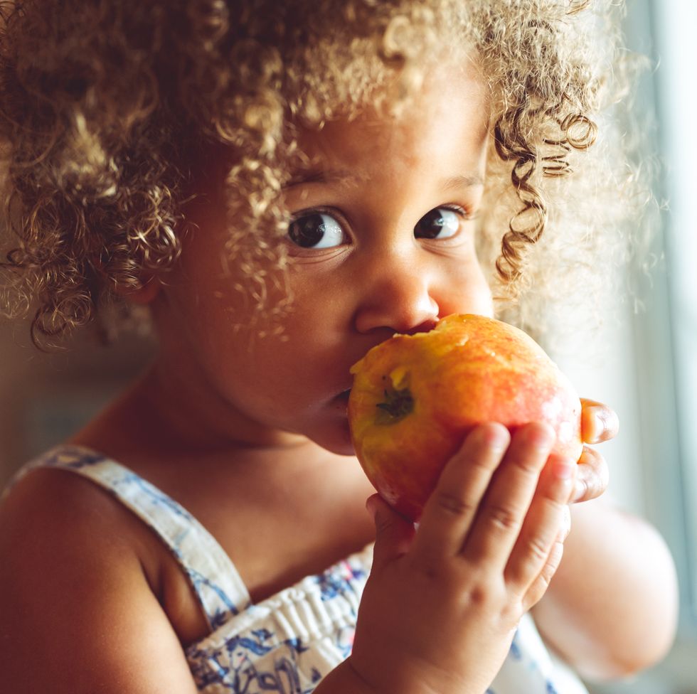 cute mixed race toddler girl eating a fresh red apple, healthy eating at home
