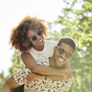 young couple enjoying piggyback ride on sunny day smiling man and woman are spending leisure time in city they are on vacation