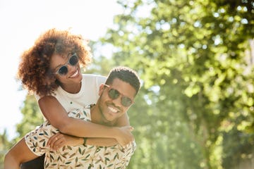 young couple enjoying piggyback ride on sunny day smiling man and woman are spending leisure time in city they are on vacation