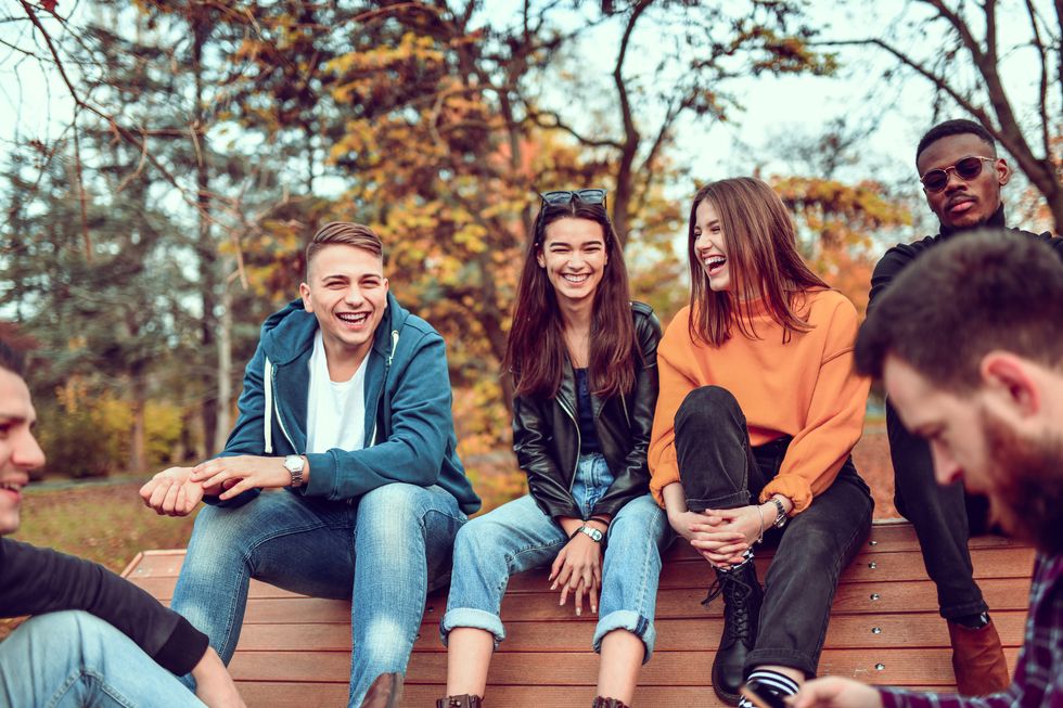 cute smiling friends sitting on park bench and relaxing during autumn