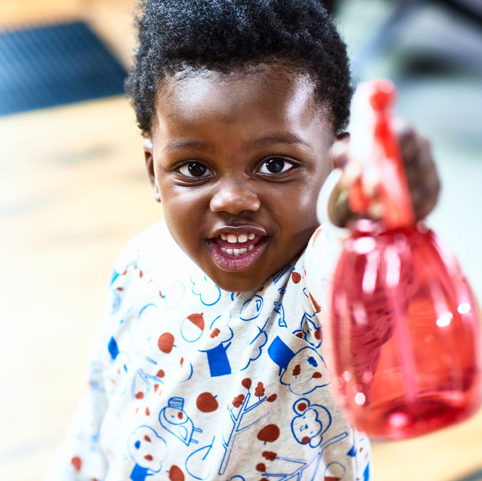 a toddler uses a red spray bottle pointed toward the camera