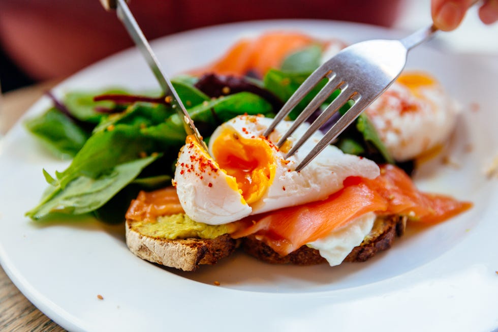 cutting poached egg on top of avocado toast with salmon