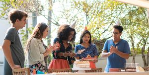 a teen happily cutting the birthday cake in front of a group of friends
