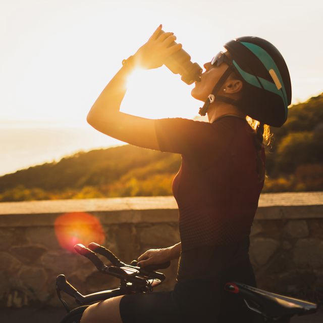 cyclist woman taking a break after riding bike and drinking water at sunset