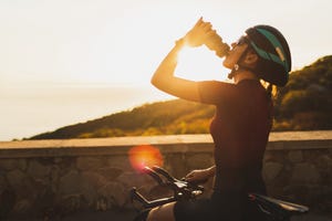 cyclist woman taking a break after riding bike and drinking water at sunset