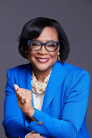 individual wearing a blue blazer with pearl jewelry posing confidently