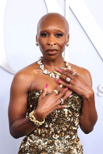 cynthia erivo wears a gold sequin dress, rests her hands against her chest and looks at the camera