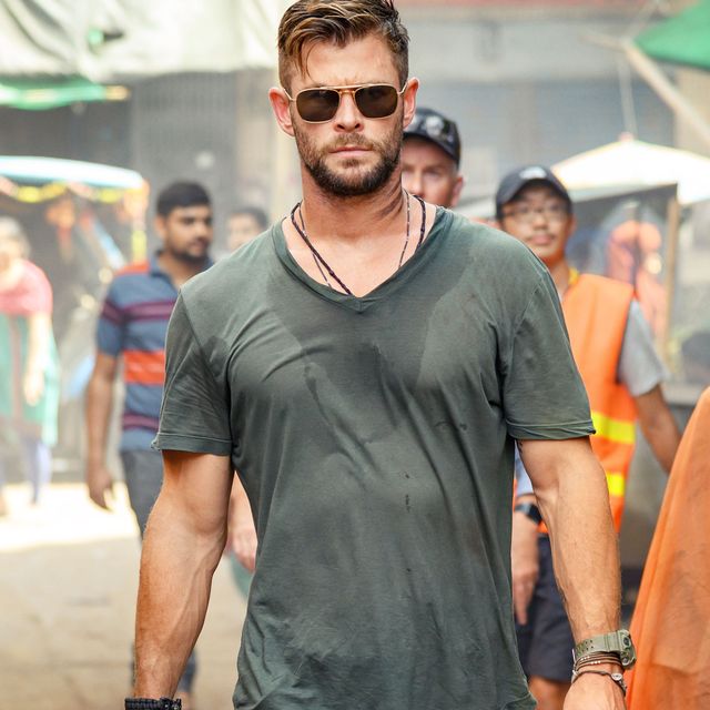 chris hemsworth in a still from netflix's extraction he's walking on a street, with a green shirt and sunglasses on
