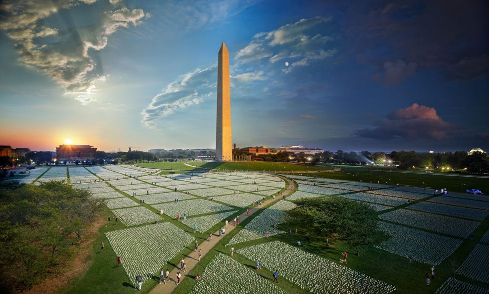 Washington D.C., United States WASHINGTON DC VERENIGDE STATENDe witte vlaggetjes die hier op de National Mall in Washington DC zijn geplant vertegenwoordigen elk een Amerikaan die aan COVID19 is overleden Toen de kunstinstallatie in september 2021 werd geopend waren er inmiddels meer dan 670000 coronadoden in het land gevallen Ruim dertig uur lang observeerde fotograaf en National Geographiconderzoeker Stephen Wilkeshoe bezoekers door de zee van witte vlaggetjes wandelden en legde daarbij afzonderlijke mensen vast die ieder voor zich de omvang van de pandemie probeerden te bevatten Als onderdeel van zijn serie Day and Night nam Wilkes 4882 fotos van de installatie en smeedde ze samen tot n enkele composietfoto