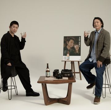 a couple of men sitting on stools in front of a table with objects on it