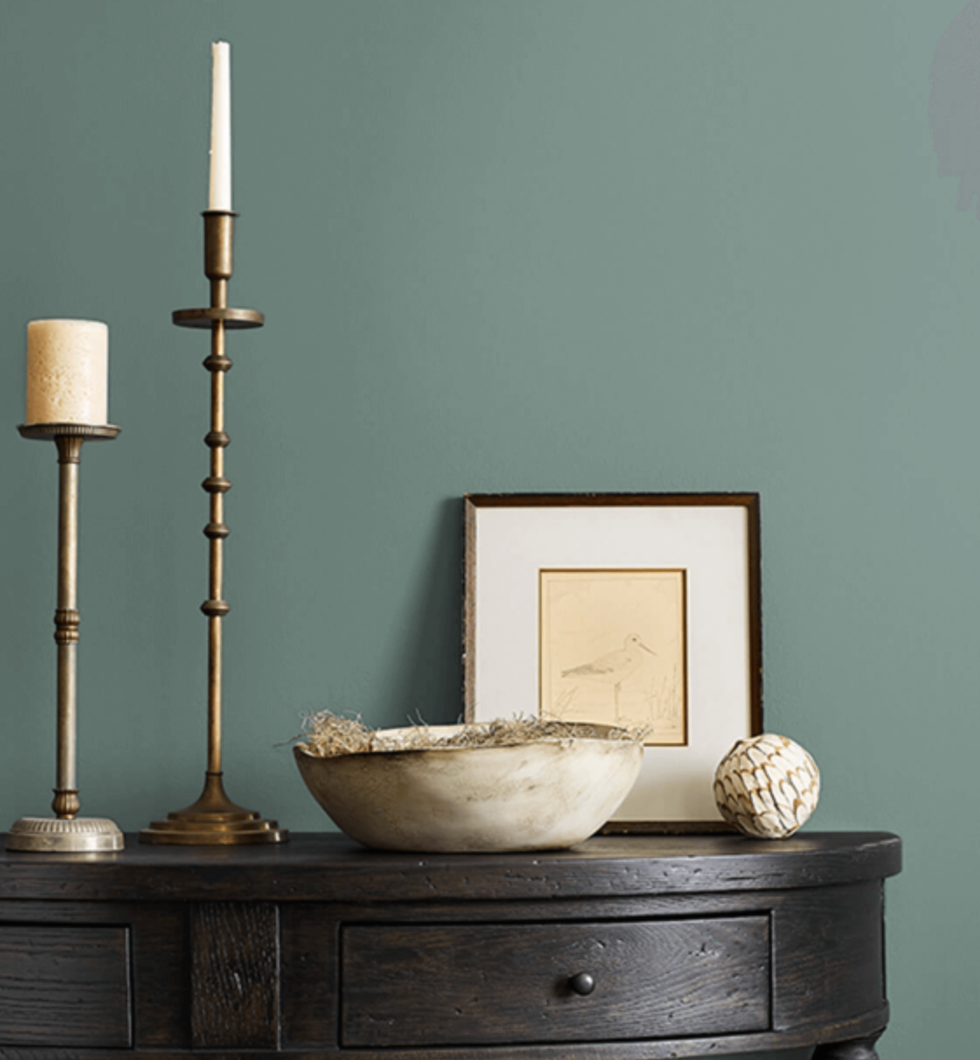 Decorative tabletop arrangement featuring a candle holder, framed artwork, a bowl with natural elements, and a textured sphere.