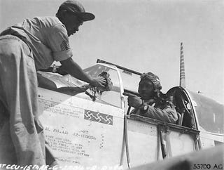 clarence lester sits in the open cockpit of a world war ii fighter plane, while an engineer works on the front of the plane