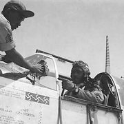 clarence lester sits in the open cockpit of a world war ii fighter plane, while an engineer works on the front of the plane