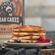 kodiak cakes box in back with stack of pancakes, syrup and fruit