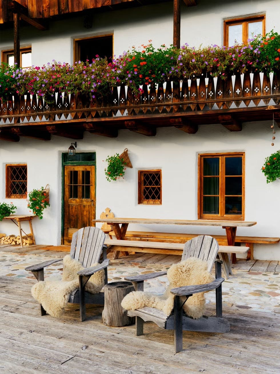 Rustic outdoor seating area in front of a wooden house with flowered balcony.