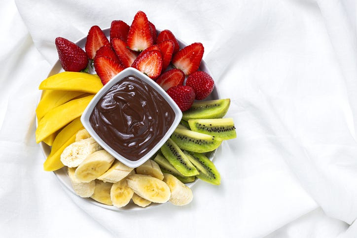 dark chocolate fondue surrounded by strawberries, mango, kiwi, banana, a healthy sweet snack
