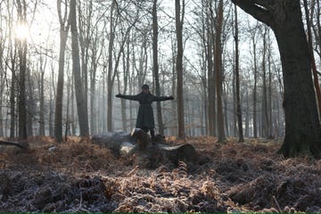 Person standing on a fallen log in a forest during early morning mist.