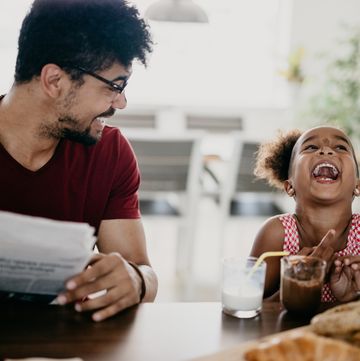 little girl bursts into laugh while having breakfast with her father