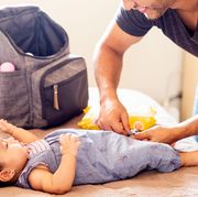 dad changing baby with diaper backpack on bed