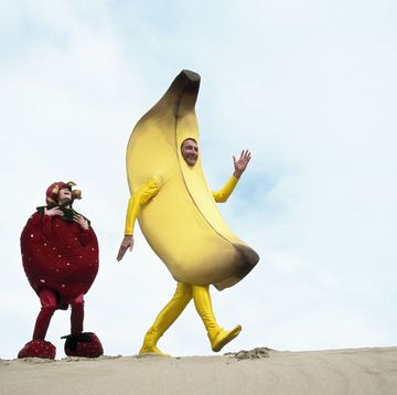 dad dressed as banana and young daughter dressed as strawberry walking beach, a photo to accompany banana peel dad joke
