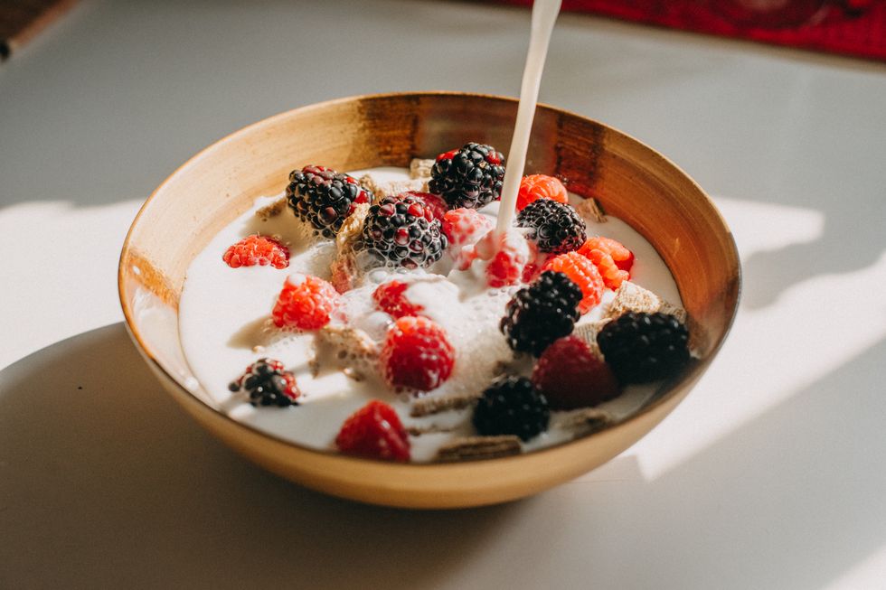 dairy free milk pouring into a bowl of whole grain cereal, raspberries and blackberries
