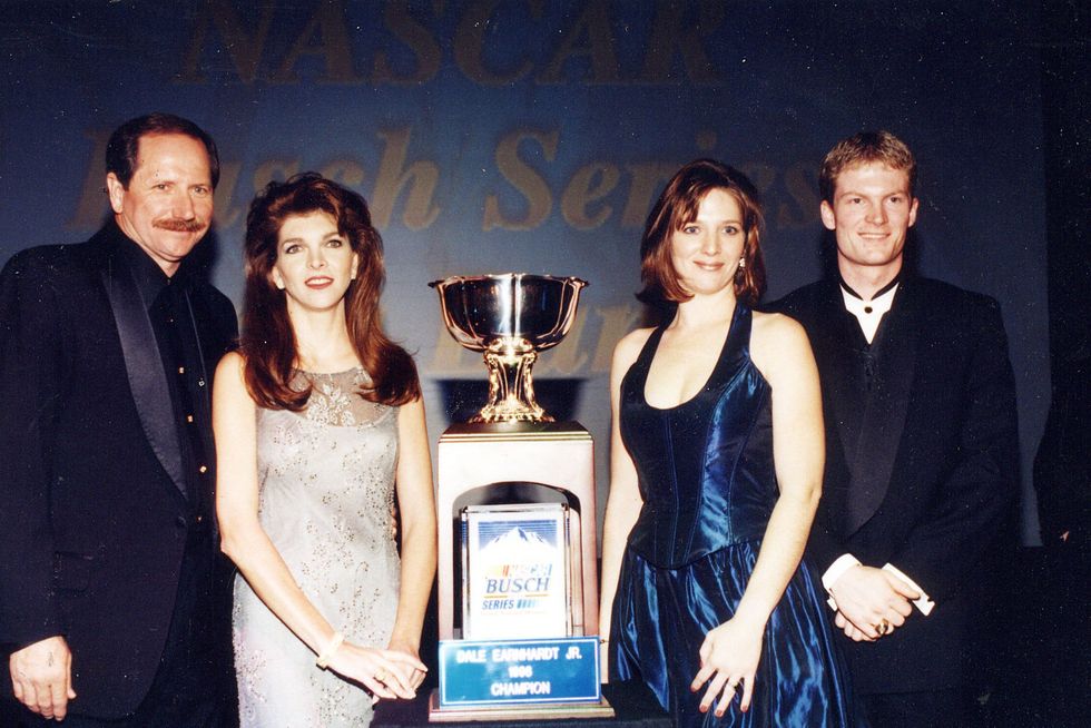 four people stand and smile for a photo, in the center is a large trophy