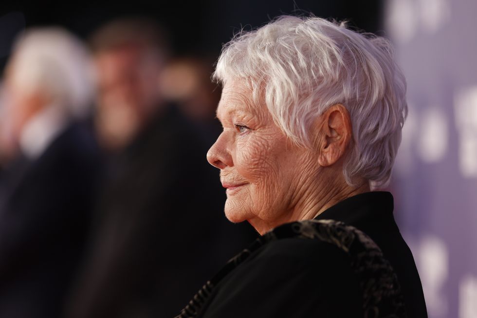 judi dench smiles while standing in profile and looking straight ahead, she wears a black outfit