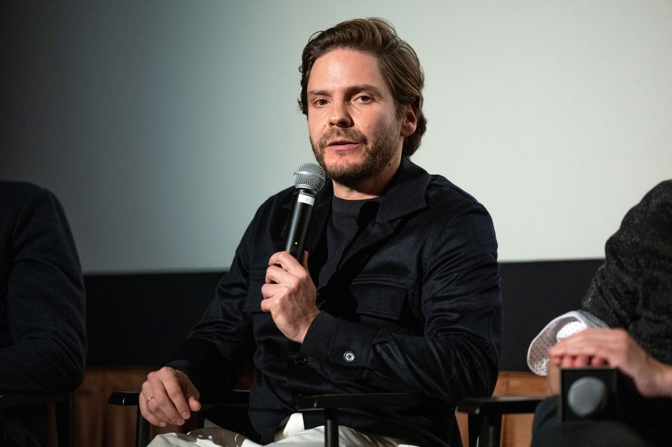 daniel brühl holds a microphone as he speaks at a press event
