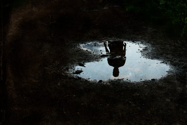 a dark, atmospheric edit of a mysterious man silhouetted in a puddle with a grunge, vintage edit