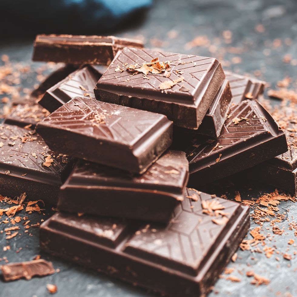 dark chocolate bar pieces on dark background with grated chocolate, pile chunks of broken chocolate