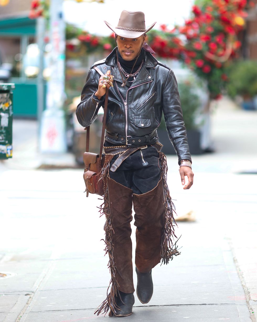 a person in a cowboy hat and leather jacket walking down a sidewalk