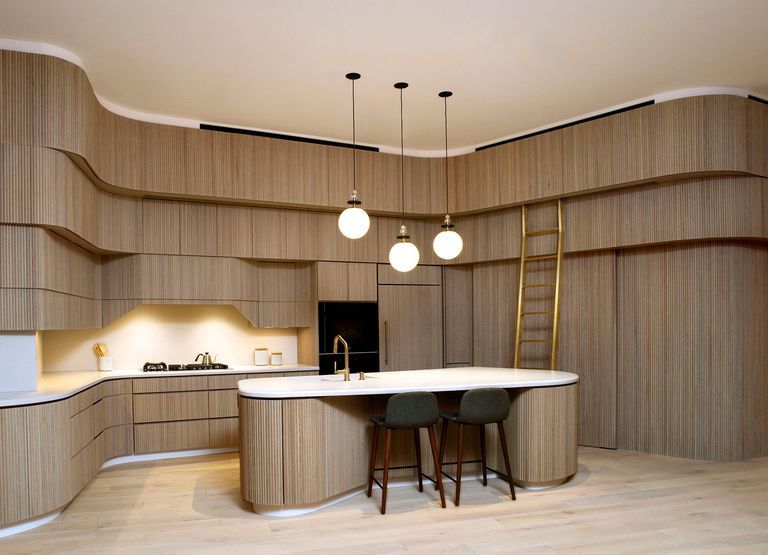 large open kitchen with curving cabinetry and matching island clad in panelling and globe pendant lights