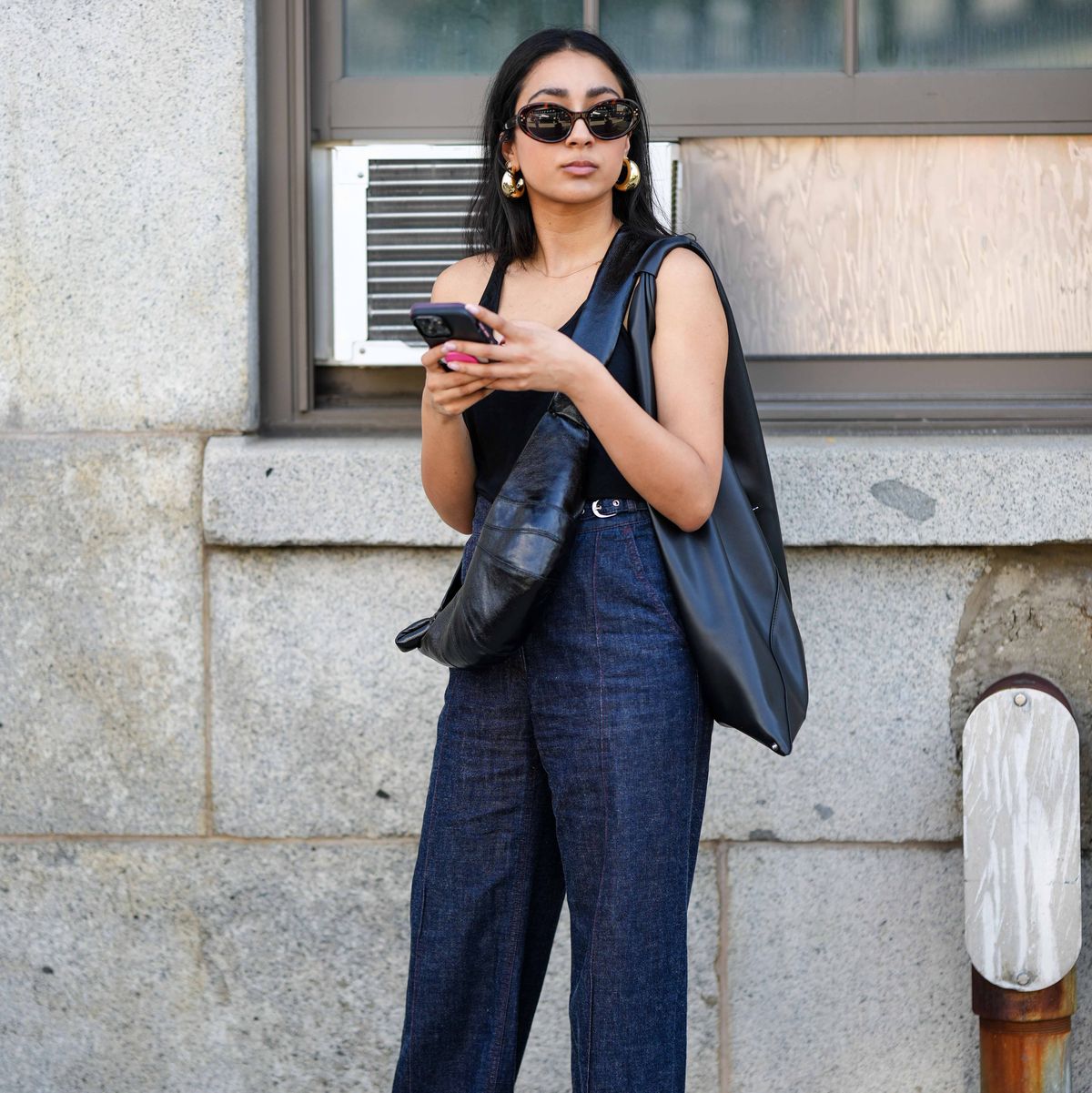 new york, new york september 12 a guest wears sunglasses, a black tank top, blue denim jeans pants, a black leather bag, golden earrings, holds a mobile phone, outside gabriela hearst, during new york fashion week, on september 12, 2023 in new york city photo by edward berthelotgetty images